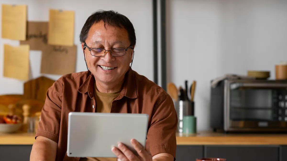 seorang lansia pria yang sedang menggengam gadget menggunakan kacamata progresif